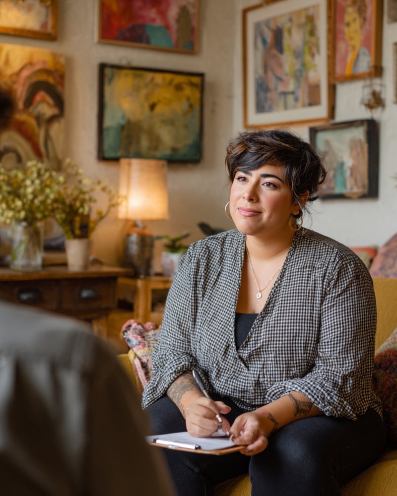BIPOC therapist in warm office with natural light, taking notes during a therapy session