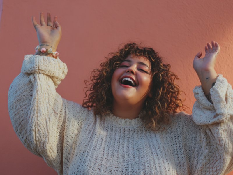 Joyful woman with curly hair laughing with arms raised against a warm coral wall — Therapy in Color photo pack