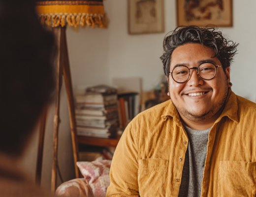 Two people in a warm therapy conversation, smiling, with cozy home-office setting